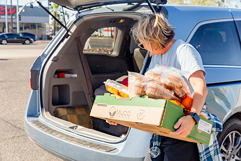 Lady loading food donations and emergency food boxes on car